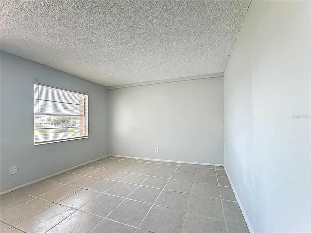 An empty room features light gray walls, a popcorn ceiling, and large square floor tiles — 694 MICHIGAN COURT UNIT 2, ST CLOUD, FL