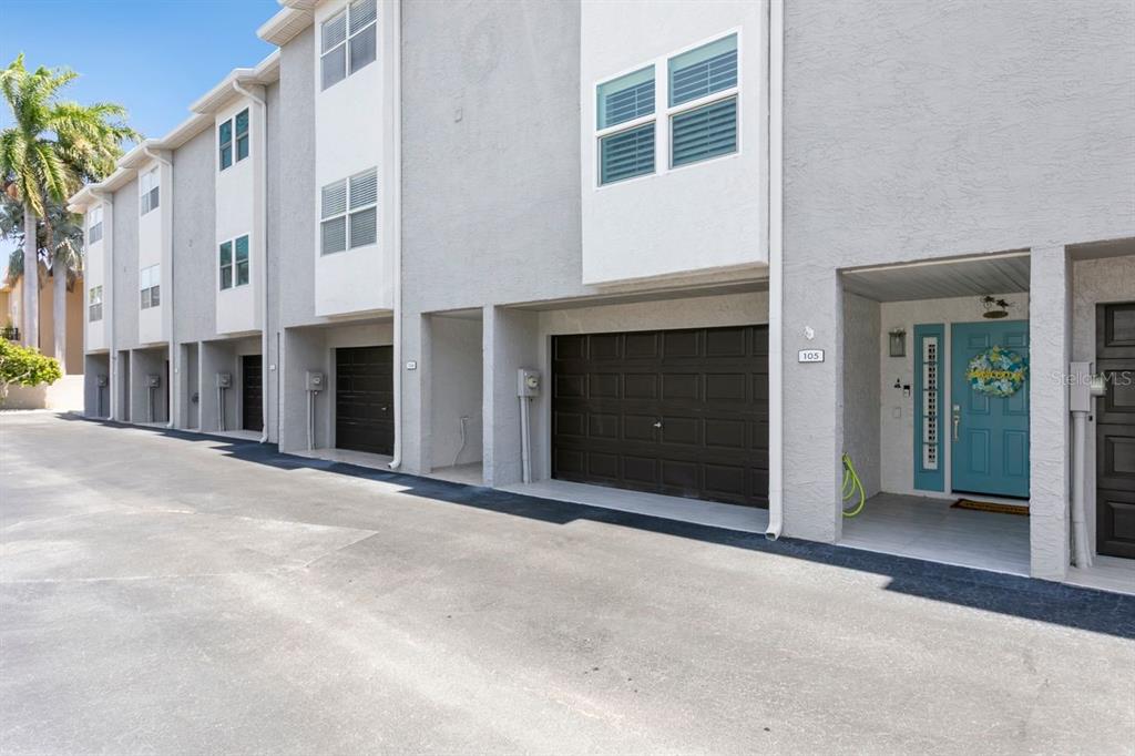 A row of multi-story townhomes with gray stucco exteriors, dark garage doors, and blue front doors — 521 PINELLAS BAYWAY S UNIT 105, TIERRA VERDE, FL