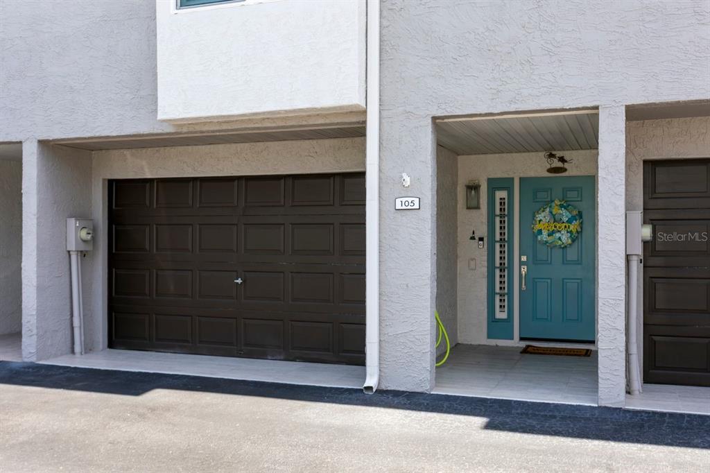 A residential exterior features a dark garage door, a teal front door, and a house number — 521 PINELLAS BAYWAY S UNIT 105, TIERRA VERDE, FL