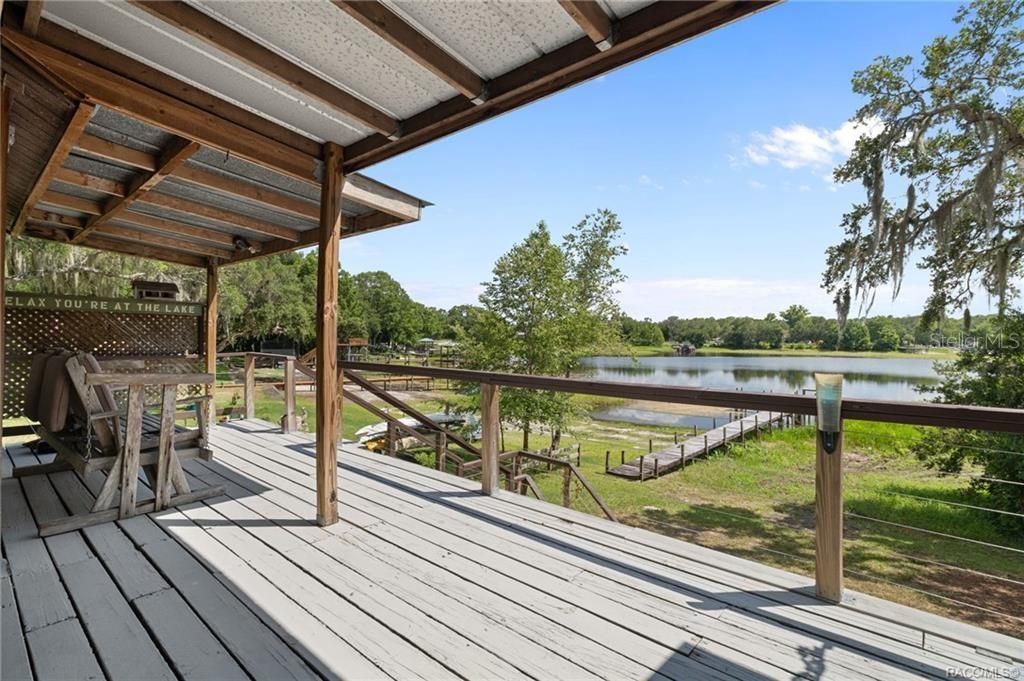 A wooden deck with a covered porch overlooks a lake and a private dock — 7514 E BROYHILL PLACE, INVERNESS, FL
