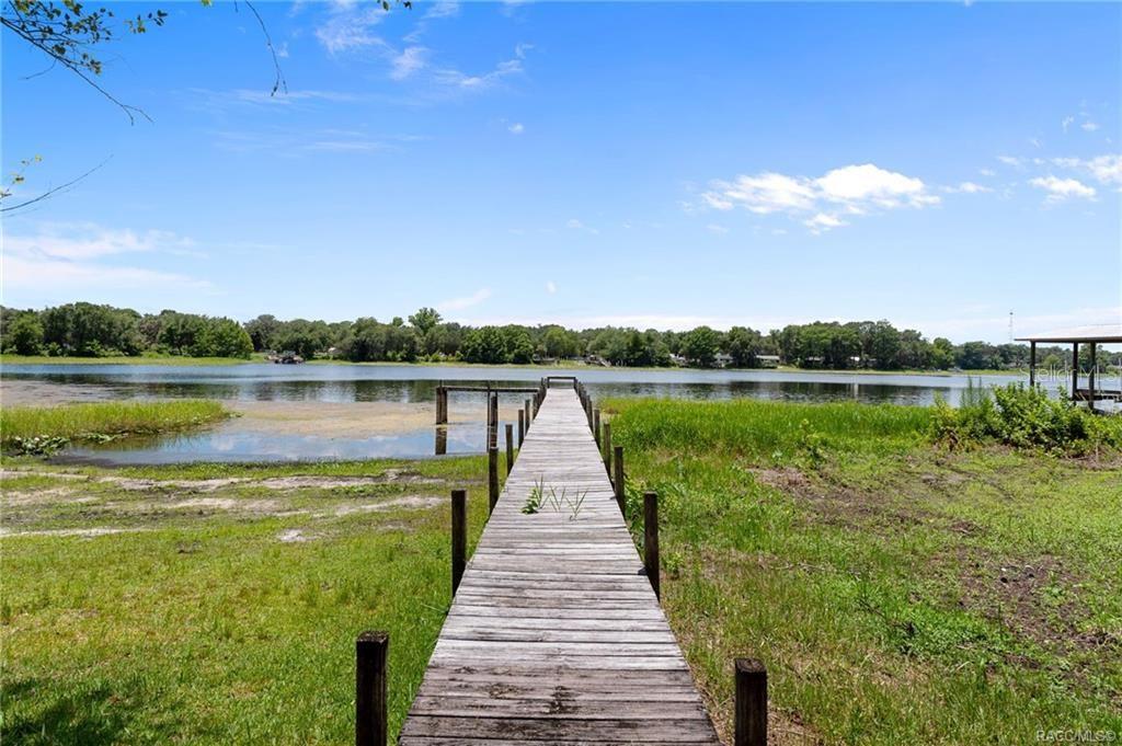 A wooden dock extends from a grassy shoreline into a calm lake under a blue sky — 7514 E BROYHILL PLACE, INVERNESS, FL