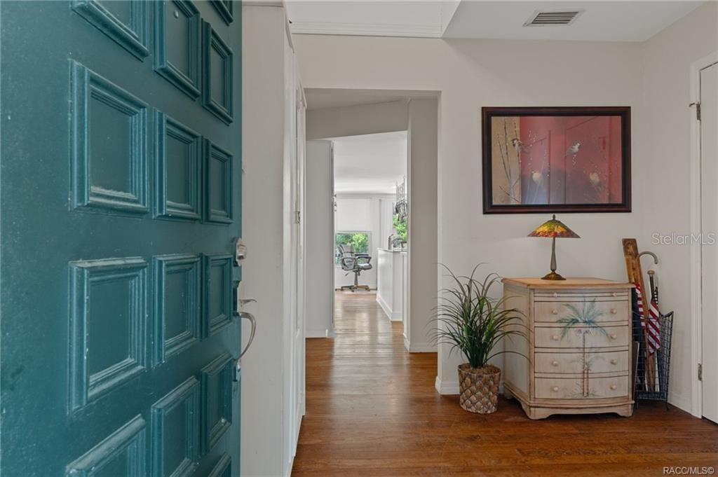 An entryway with a teal door, hardwood floors, a small chest, and a framed painting — 7514 E BROYHILL PLACE, INVERNESS, FL