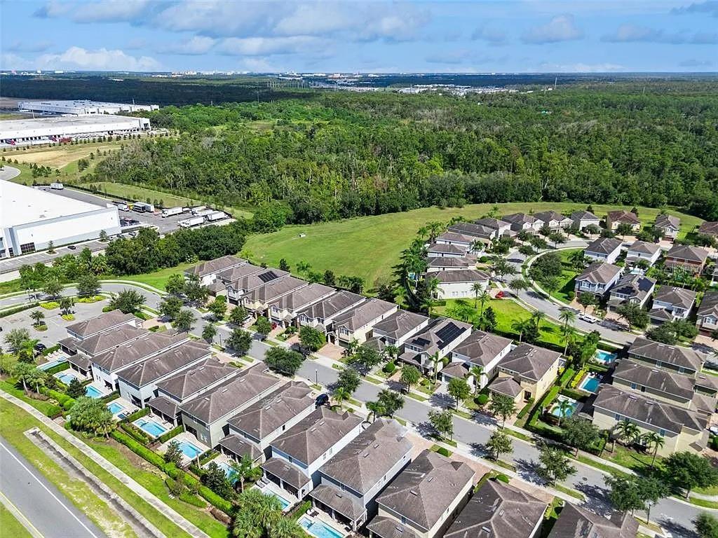 An aerial view shows a suburban neighborhood with houses, swimming pools, and nearby industrial buildings — 310 PENDANT COURT, KISSIMMEE, FL