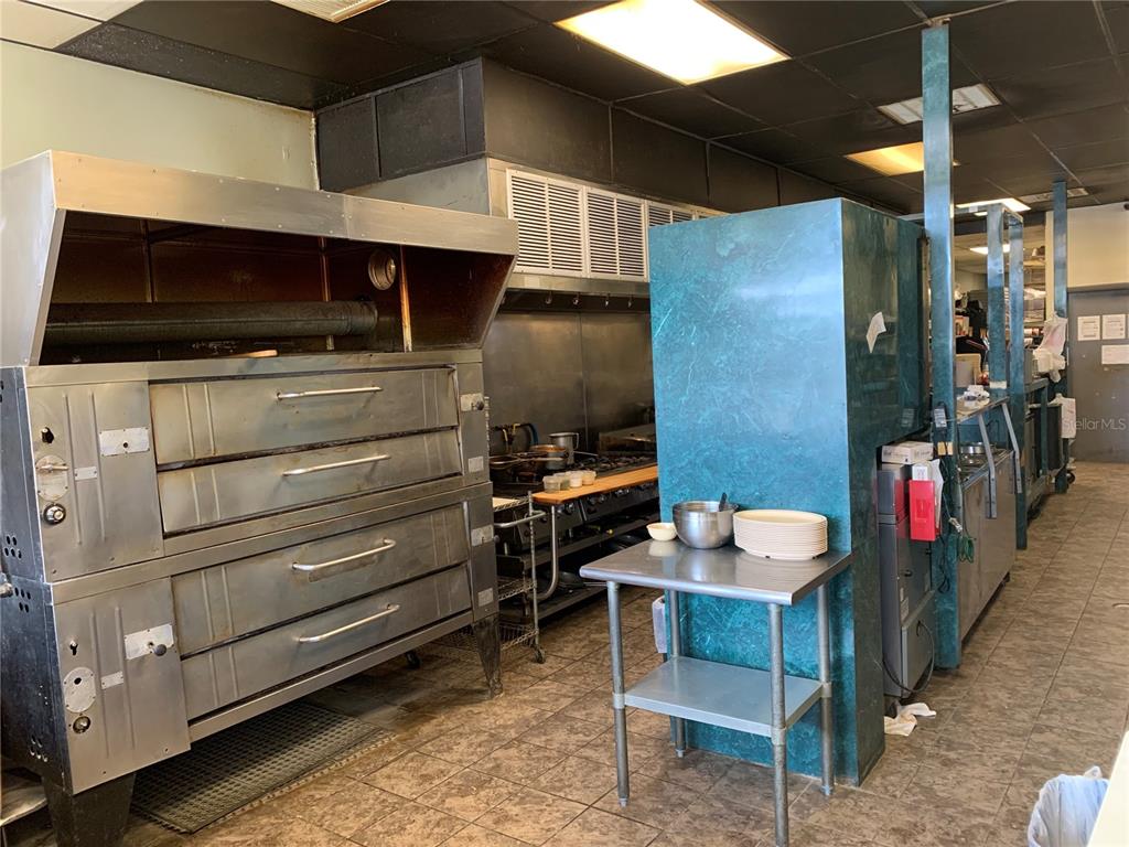 A commercial kitchen features a large stainless steel oven, a stove, and metal prep tables — 2110 SARNO ROAD, MELBOURNE, FL