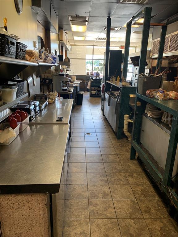 A commercial kitchen features stainless steel prep tables, tiled flooring, and open shelving — 2110 SARNO ROAD, MELBOURNE, FL