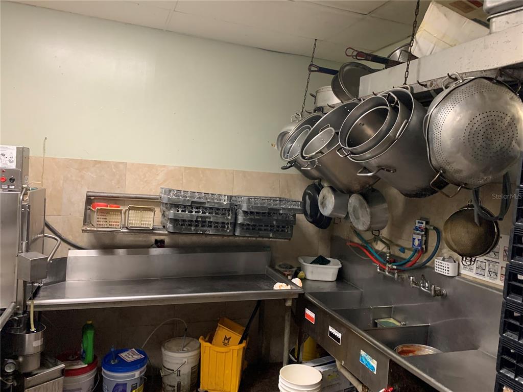 A commercial kitchen features stainless steel sinks, hanging pots, and stacked dish racks — 2110 SARNO ROAD, MELBOURNE, FL