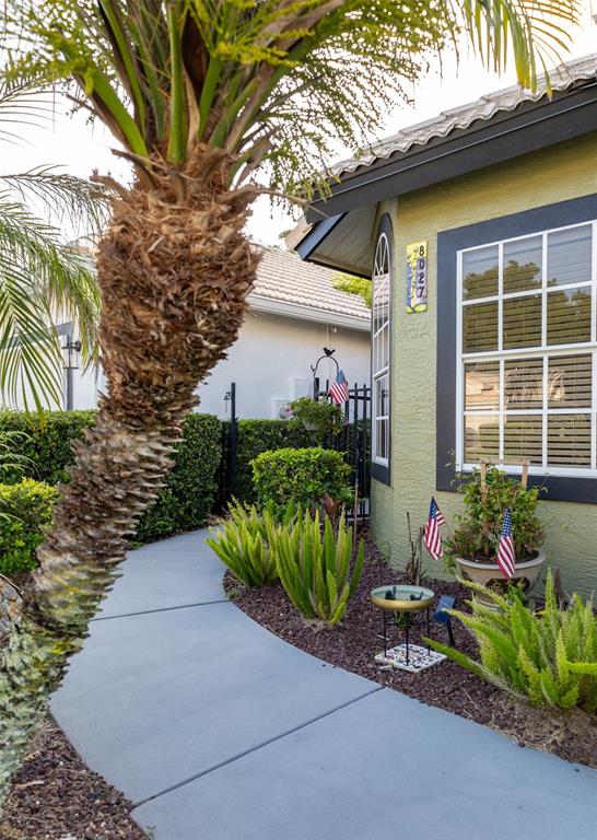 A curved concrete walkway leads to the entrance of a house with green stucco siding — 8027 SAINT ANDREWS WAY, MOUNT DORA, FL