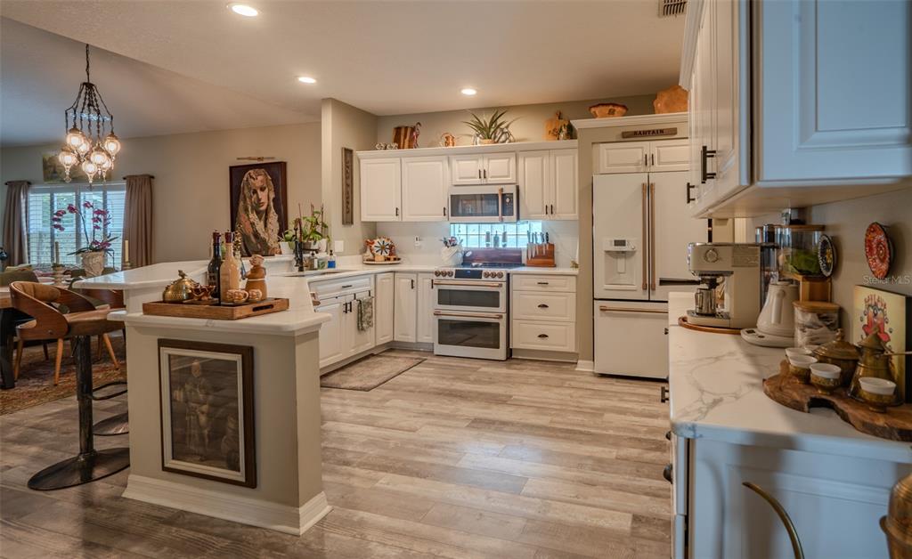 A kitchen features white cabinetry, stainless steel appliances, and light wood-look flooring — 8027 SAINT ANDREWS WAY, MOUNT DORA, FL
