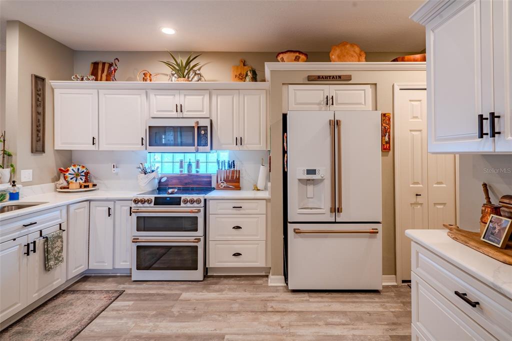 A kitchen features white cabinets, stainless steel appliances, and wood-look flooring — 8027 SAINT ANDREWS WAY, MOUNT DORA, FL
