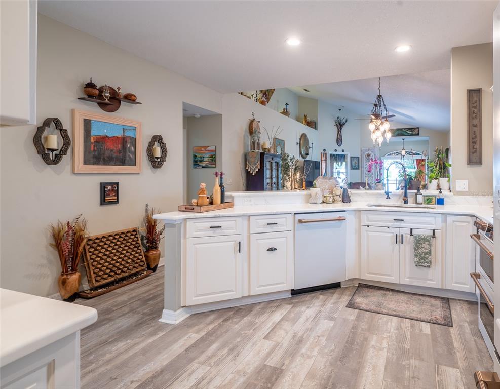 A kitchen with white cabinets, light wood-look flooring, and a view into an adjacent living area — 8027 SAINT ANDREWS WAY, MOUNT DORA, FL