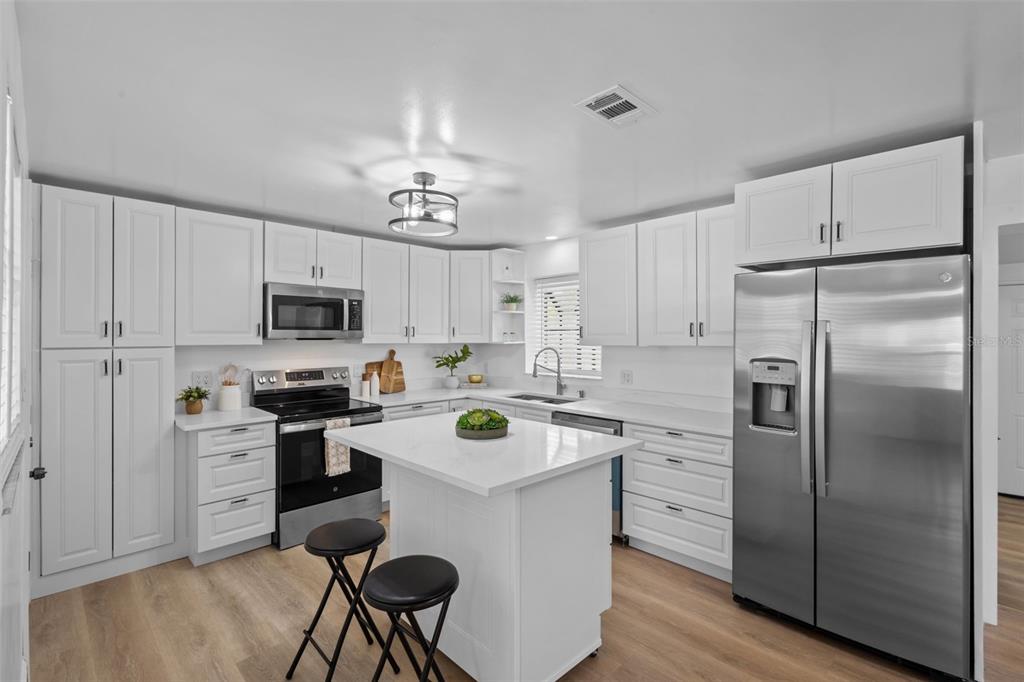 A modern kitchen features white cabinetry, stainless steel appliances, a center island, and wood flooring — 1781 APACHE TRAIL, CLEARWATER, FL