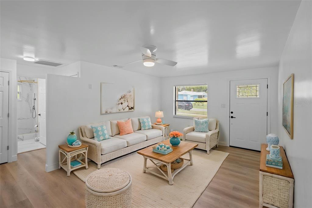 A bright living room features light wood flooring, white walls, and a ceiling fan — 1781 APACHE TRAIL, CLEARWATER, FL