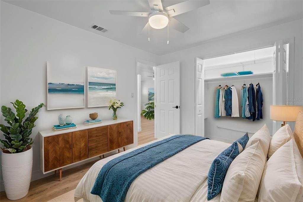 A bedroom features a bed with blue accents, a walk-in closet, and light wood flooring — 1781 APACHE TRAIL, CLEARWATER, FL