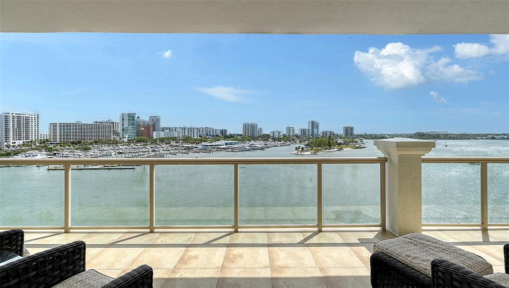 A balcony with tiled flooring and glass railings overlooks a marina and city skyline — 464 GOLDEN GATE POINT UNIT 702, SARASOTA, FL