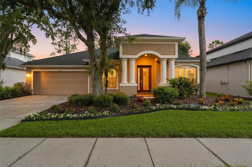A single-story house with a tan stucco exterior, a two-car garage, and a columned entryway — 27417 SILVER THATCH DRIVE, WESLEY CHAPEL, FL