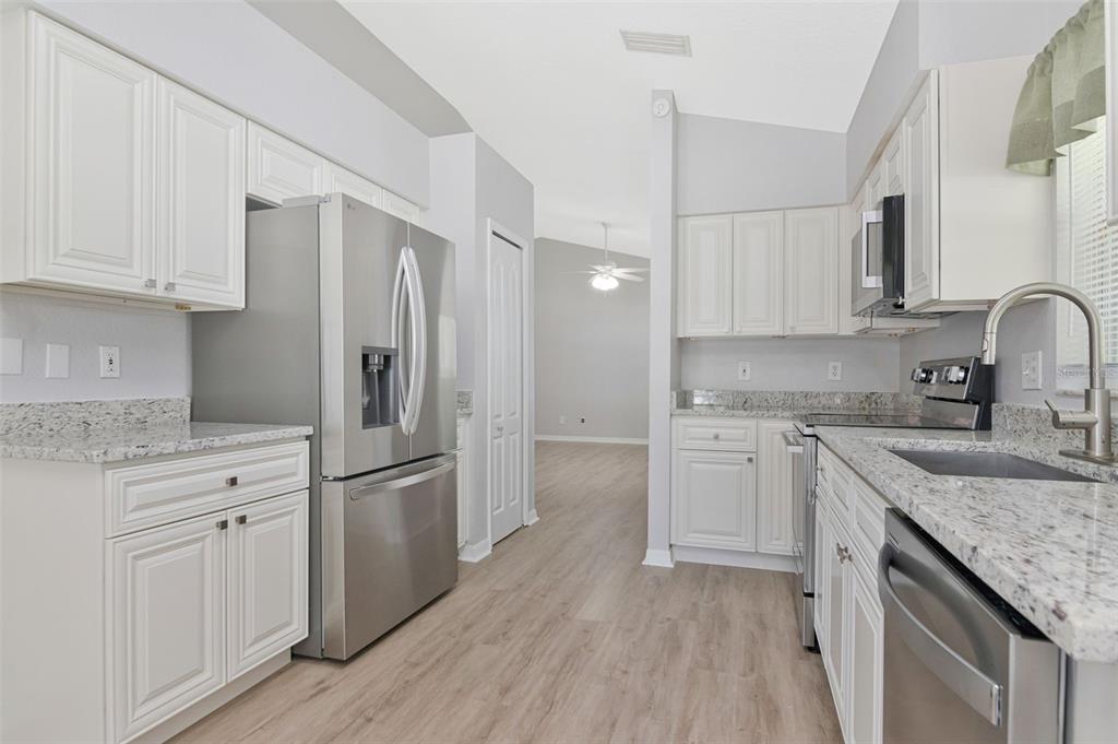 A kitchen with white cabinets, granite countertops, stainless steel appliances, and light wood-look flooring — 1914 BRANDON BROOK ROAD, VALRICO, FL