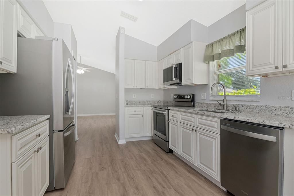A kitchen with white cabinets, granite countertops, stainless steel appliances, and light wood-look flooring — 1914 BRANDON BROOK ROAD, VALRICO, FL