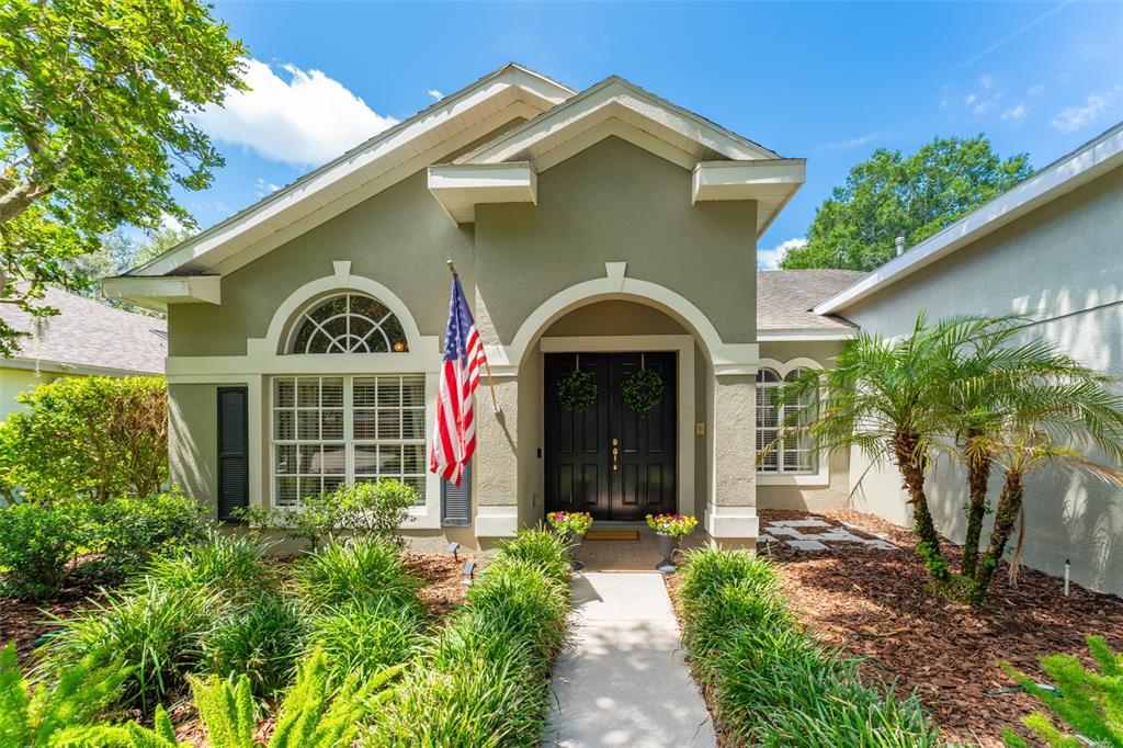 A single-story house with a green stucco exterior, arched windows, and a black double front door — 15211 MERLINGLEN PLACE, LITHIA, FL