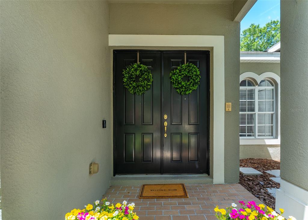A front entryway features black double doors with green wreaths and a brick porch — 15211 MERLINGLEN PLACE, LITHIA, FL