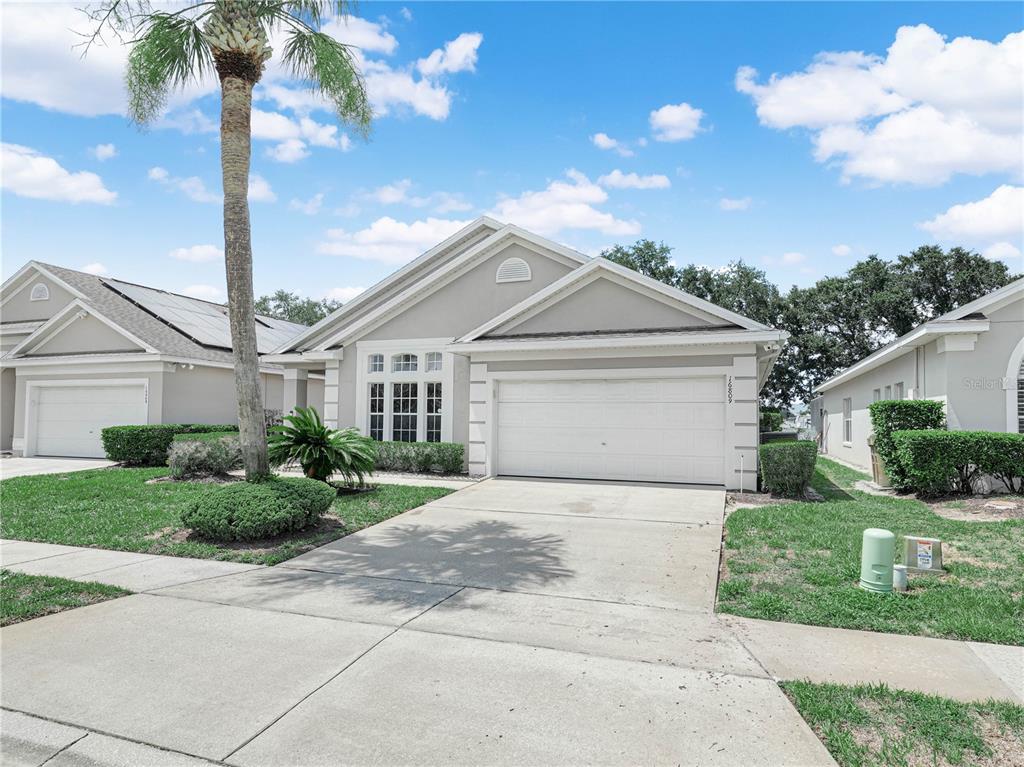 A single-story suburban house with a white garage, beige siding, and a palm tree — 16809 GLENBROOK BOULEVARD, CLERMONT, FL