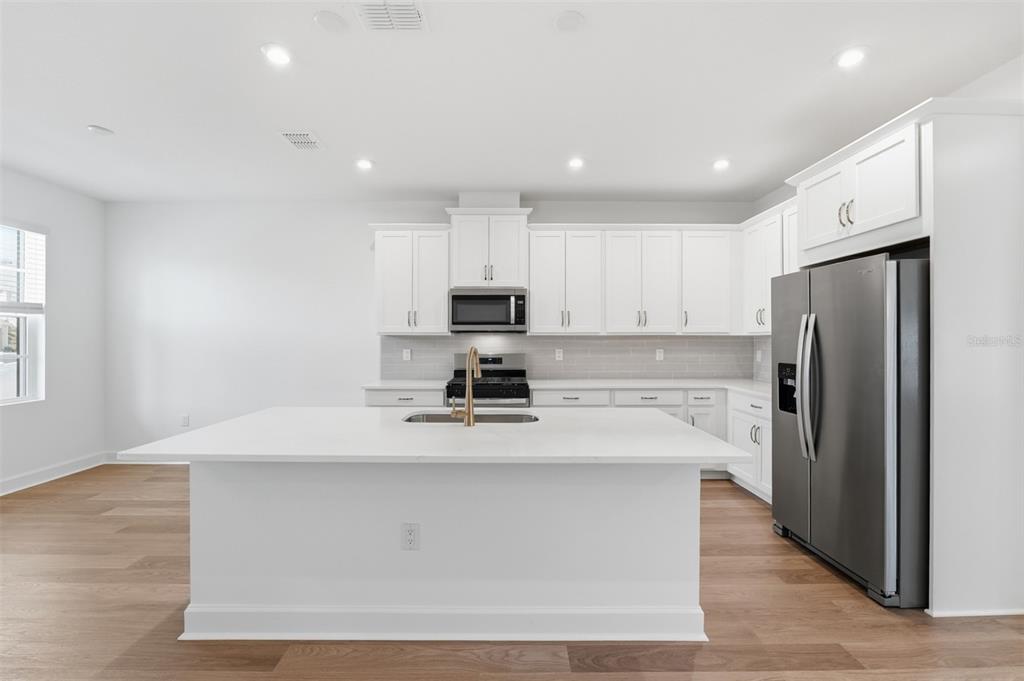 A modern kitchen features white cabinetry, a large central island, and stainless steel appliances — 1883 SEAWALL WAY, CELEBRATION, FL