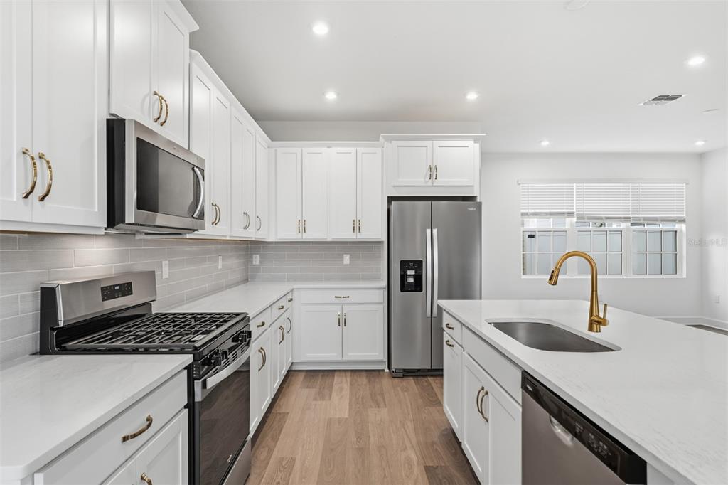 A modern kitchen features white cabinets, stainless steel appliances, a kitchen island, and wood flooring — 1883 SEAWALL WAY, CELEBRATION, FL