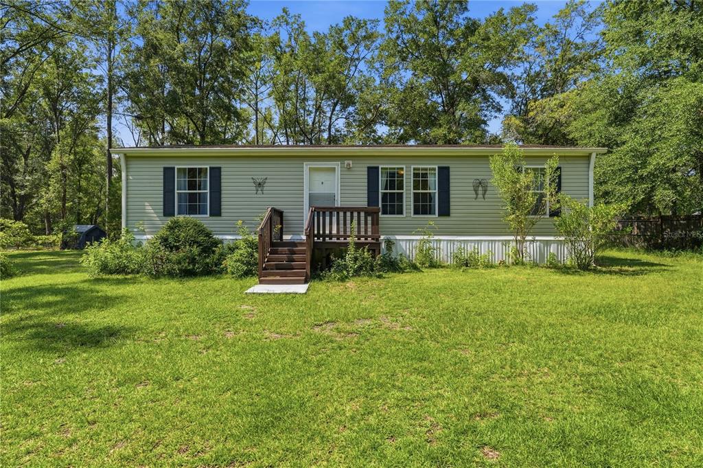 A single-story manufactured home with light green siding and a small wooden front porch — 24628 NW 84TH PLACE, ALACHUA, FL