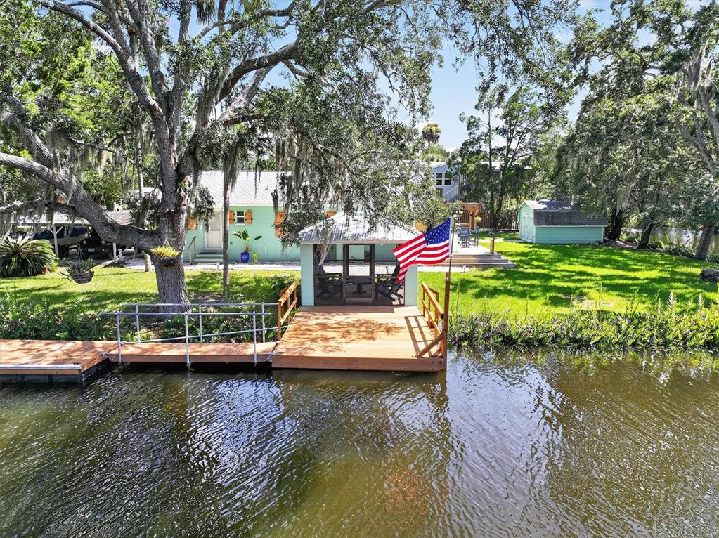 A waterfront home with a wooden dock, screened gazebo, and American flag on a grassy lawn — 6086 ISLAND DRIVE, WEEKI WACHEE, FL
