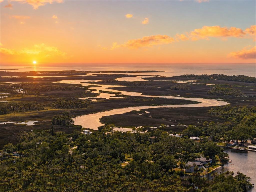 An aerial view of a winding river flowing through marshland toward a sunset over the ocean — 6086 ISLAND DRIVE, WEEKI WACHEE, FL