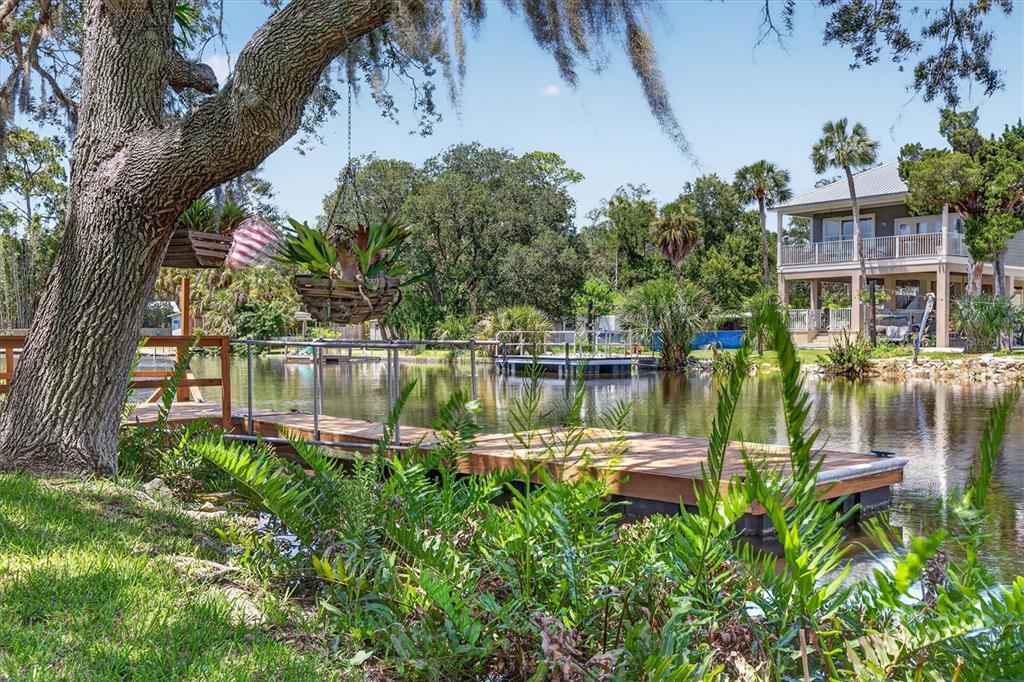 A wooden dock extends into a calm canal in front of a two-story house — 6086 ISLAND DRIVE, WEEKI WACHEE, FL