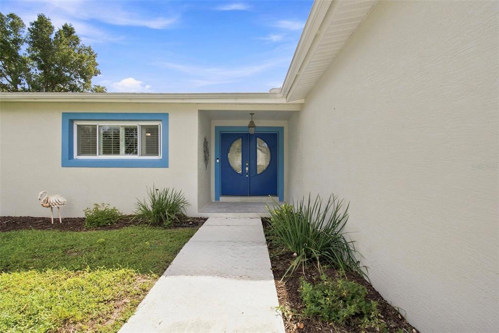 A concrete walkway leads to a blue double front door on a white house exterior — 1303 SE KINGS BAY DRIVE, CRYSTAL RIVER, FL
