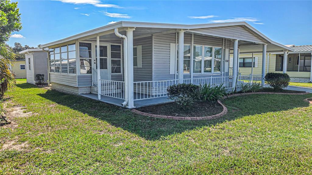 A single-story manufactured home with grey siding, a covered porch, and a landscaped front yard — 5638 BENTON STREET, ZEPHYRHILLS, FL