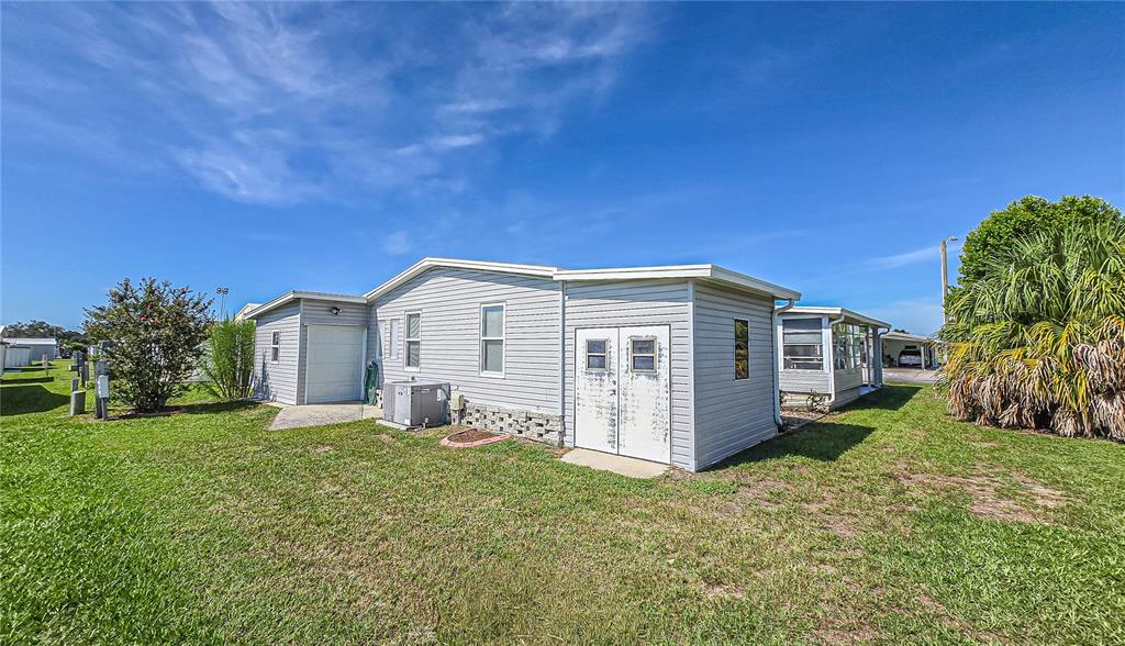 The exterior of a light gray manufactured home features a small garage and storage doors — 5638 BENTON STREET, ZEPHYRHILLS, FL