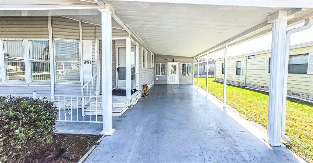 A covered carport leads to the front entrance of a mobile home with white columns — 5638 BENTON STREET, ZEPHYRHILLS, FL