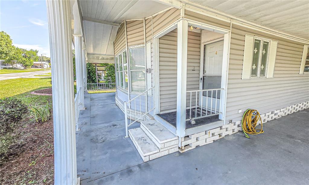 A covered porch with concrete flooring, white columns, and steps leading to a front door — 5638 BENTON STREET, ZEPHYRHILLS, FL