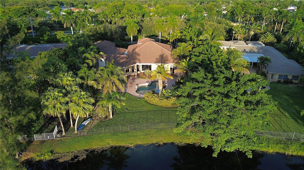 An aerial view shows a house with a tiled roof, pool, and backyard facing a lake — 471 RANCH ROAD, WESTON, FL