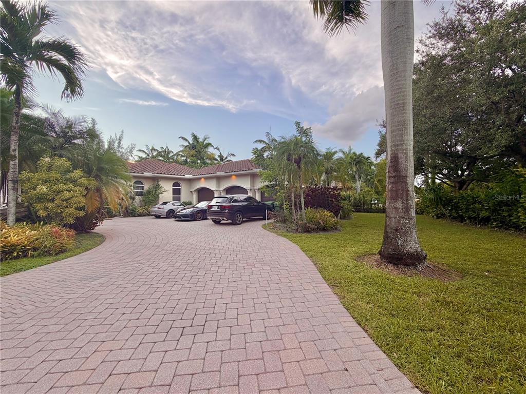 A paved driveway leads to a house with a three-car garage and tropical landscaping — 471 RANCH ROAD, WESTON, FL