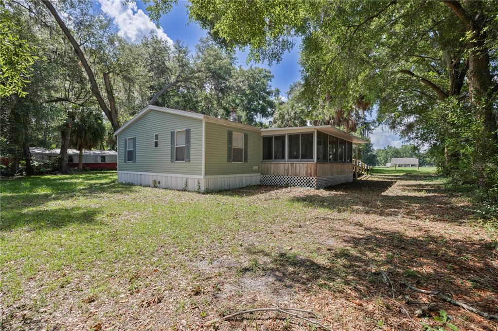 A light green manufactured home with a screened-in porch sits on a grassy, wooded lot — 2786 NE 33RD PLACE, COLEMAN, FL