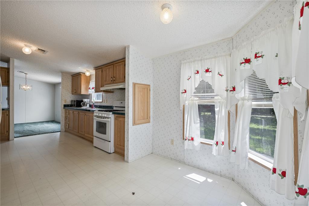 A kitchen and dining area with wood cabinets, white appliances, and apple-patterned curtains — 2786 NE 33RD PLACE, COLEMAN, FL