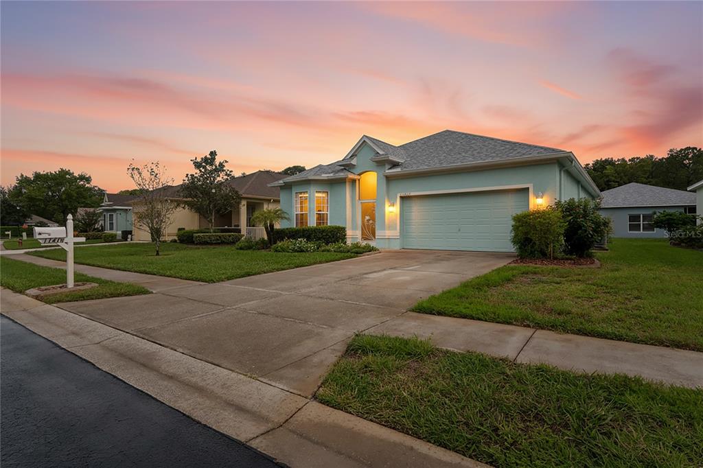 A light blue single-story house with a two-car garage sits under a sunset sky — 11415 WINDSTAR COURT, NEW PORT RICHEY, FL