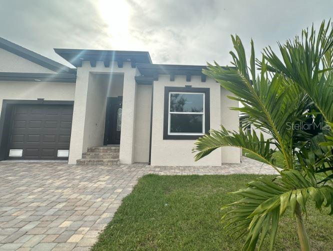 The exterior of a modern house features a paved driveway, a garage, and a palm tree — 57 BOUNDARY BOULEVARD UNIT 2, ROTONDA WEST, FL