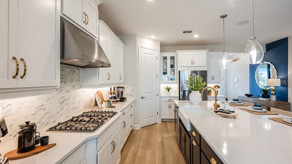 A kitchen features a blue island, white cabinetry, and a dining table in the foreground — 7800 CENTAURUS WAY, SARASOTA, FL