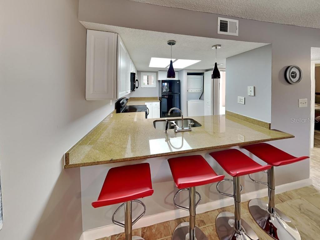 A kitchen features a granite breakfast bar with three red stools and white cabinetry — 4250 A1A S UNIT K12, ST AUGUSTINE, FL