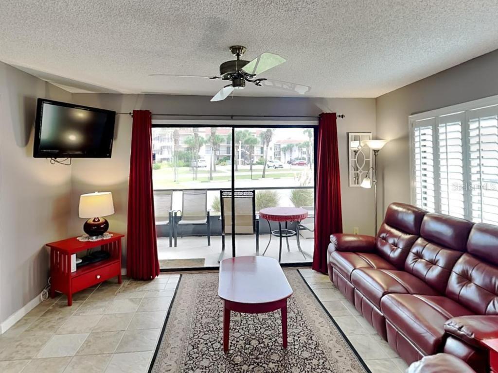 A living room features a red sofa, matching coffee table, tile flooring, and a sliding glass door — 4250 A1A S UNIT K12, ST AUGUSTINE, FL