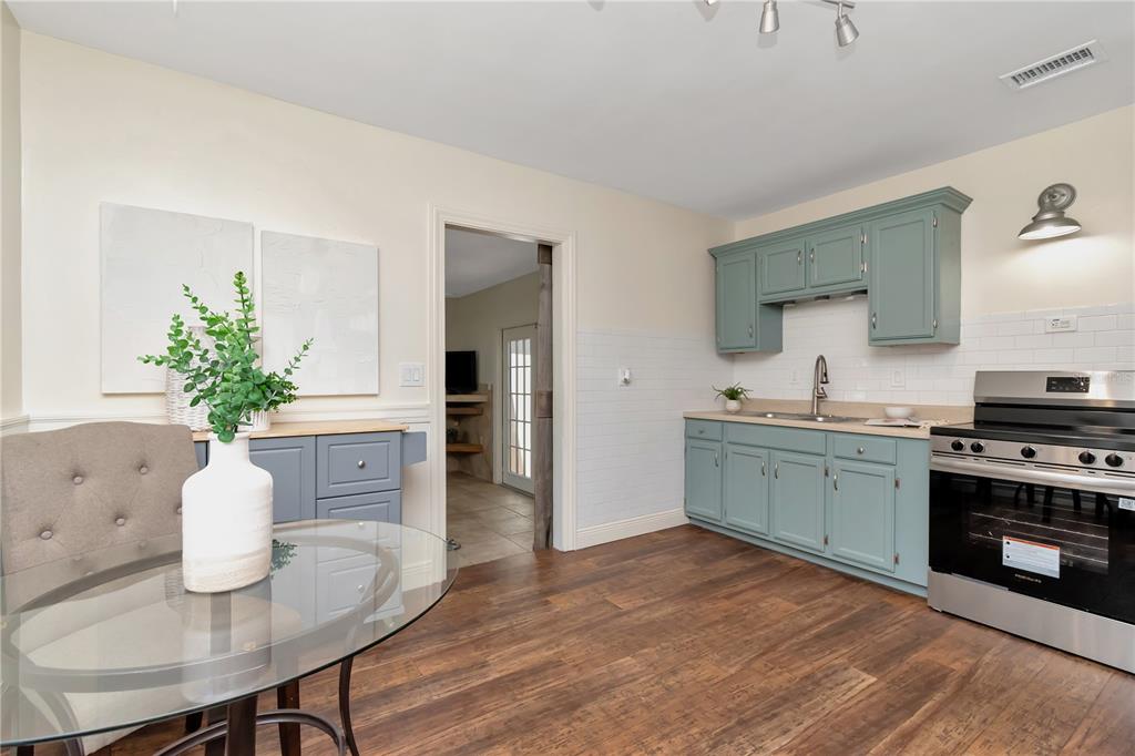 A kitchen features blue cabinets, a stainless steel stove, and a glass-topped dining table — 1419 55TH STREET S, GULFPORT, FL