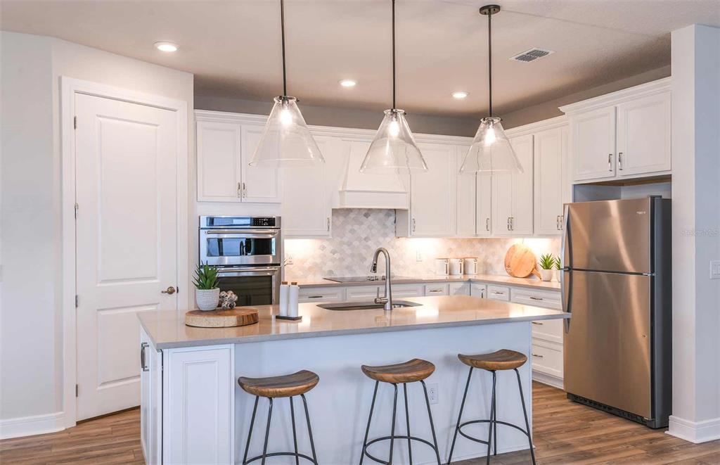 A modern kitchen features white cabinetry, a central island with bar stools, and stainless appliances — 13585 CANYON RIDGE ROAD, SPRING HILL, FL