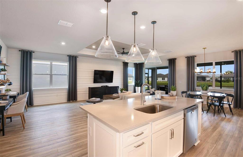 An open-concept kitchen and living area featuring white cabinetry, pendant lighting, and wood-look flooring — 13585 CANYON RIDGE ROAD, SPRING HILL, FL