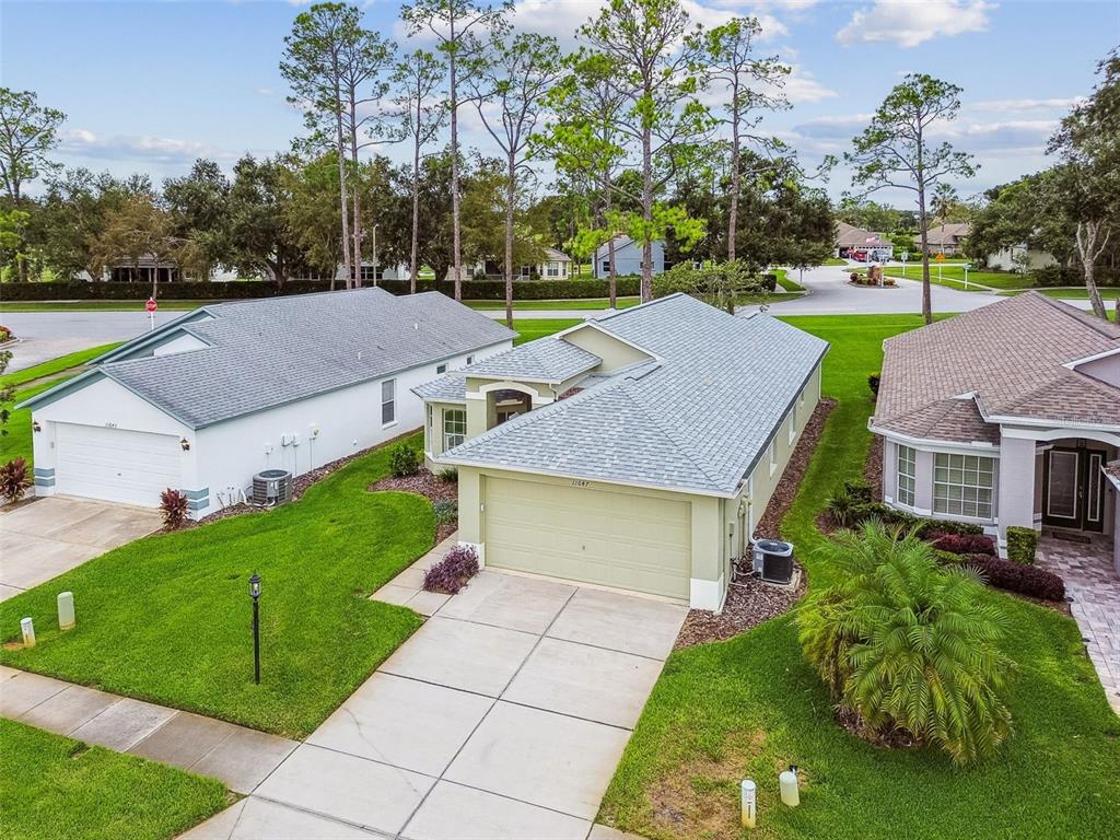 An aerial view shows a suburban house with a light green exterior and a gray roof — 11647 WHEATFIELD LOOP, HUDSON, FL