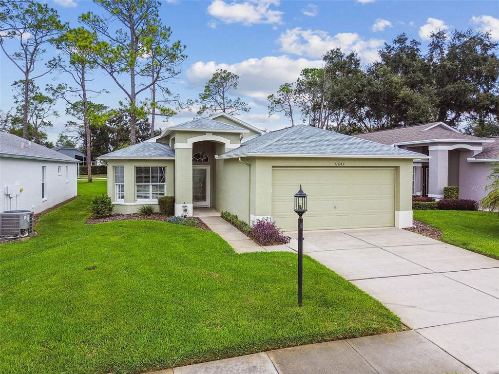 A light green single-story suburban house with a two-car garage and a front walkway — 11647 WHEATFIELD LOOP, HUDSON, FL