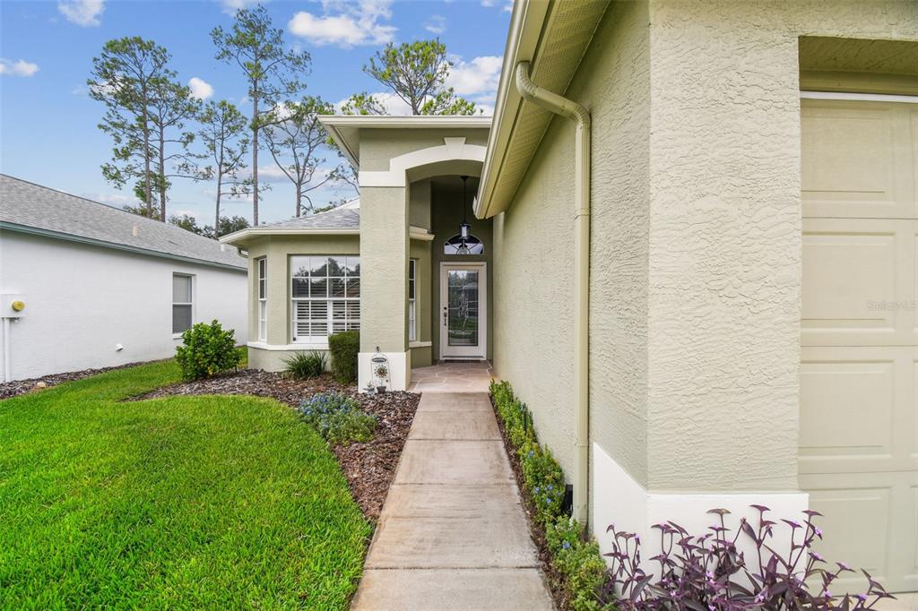 A concrete walkway leads to the front entrance of a light green stucco house — 11647 WHEATFIELD LOOP, HUDSON, FL